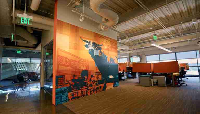 Interior office space with exposed ceiling and a large orange wall graphic featuring an illustrated bull and bold lettering, by Capital Sign Solutions