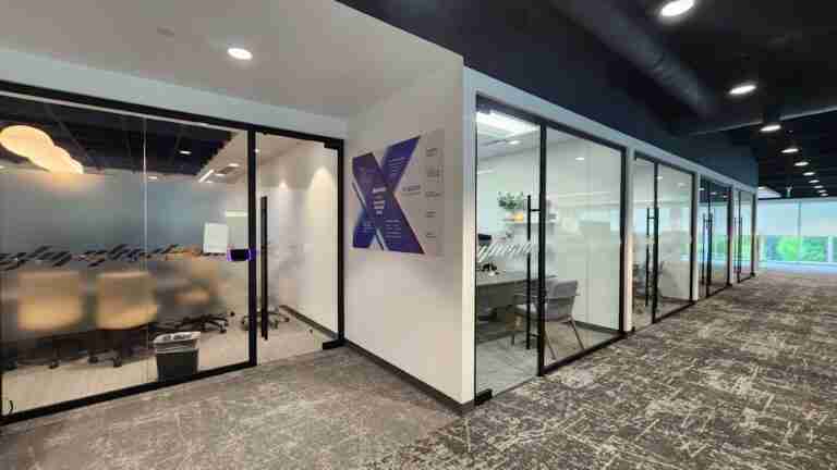 Modern office corridor with glass-walled meeting rooms and a purple angular wall graphic reading Baxter, interior signage, by Capital Sign Solutions