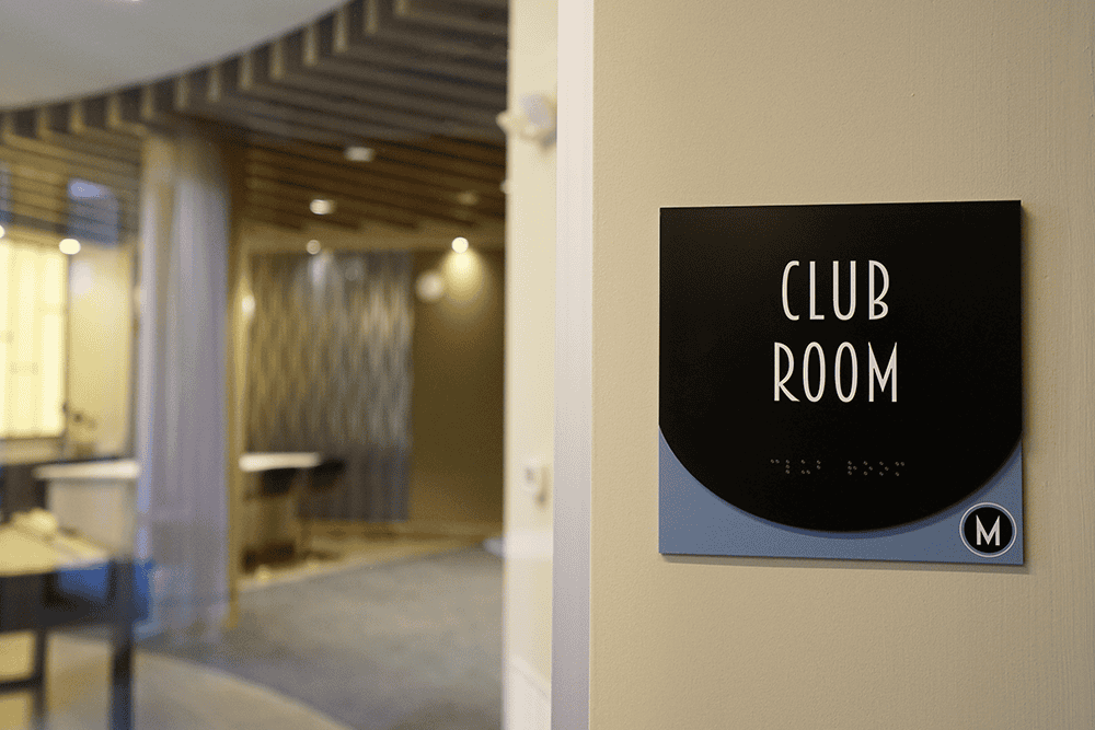Black ADA-compliant Club Room sign with raised braille lettering mounted on an interior wall, by Capital Sign Solutions